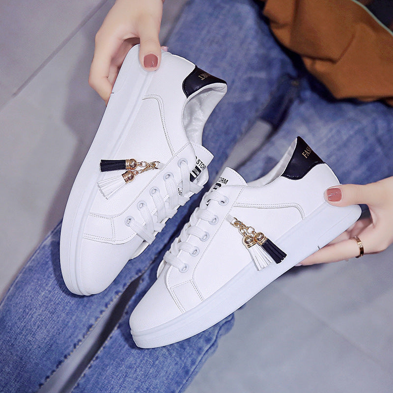 White low-top sneakers with black heel accents and gold tassel charm, lace-up.