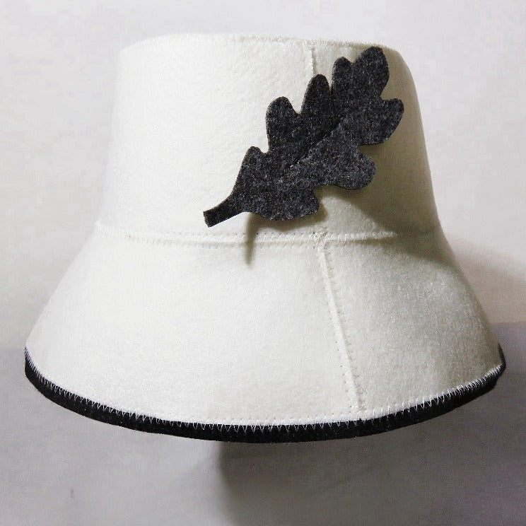 White wool bucket hat with dark leaf applique on front and dark stitched brim edge