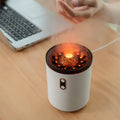 Aroma diffuser humidifier, white cylinder with orange flame-lit top on wood desk