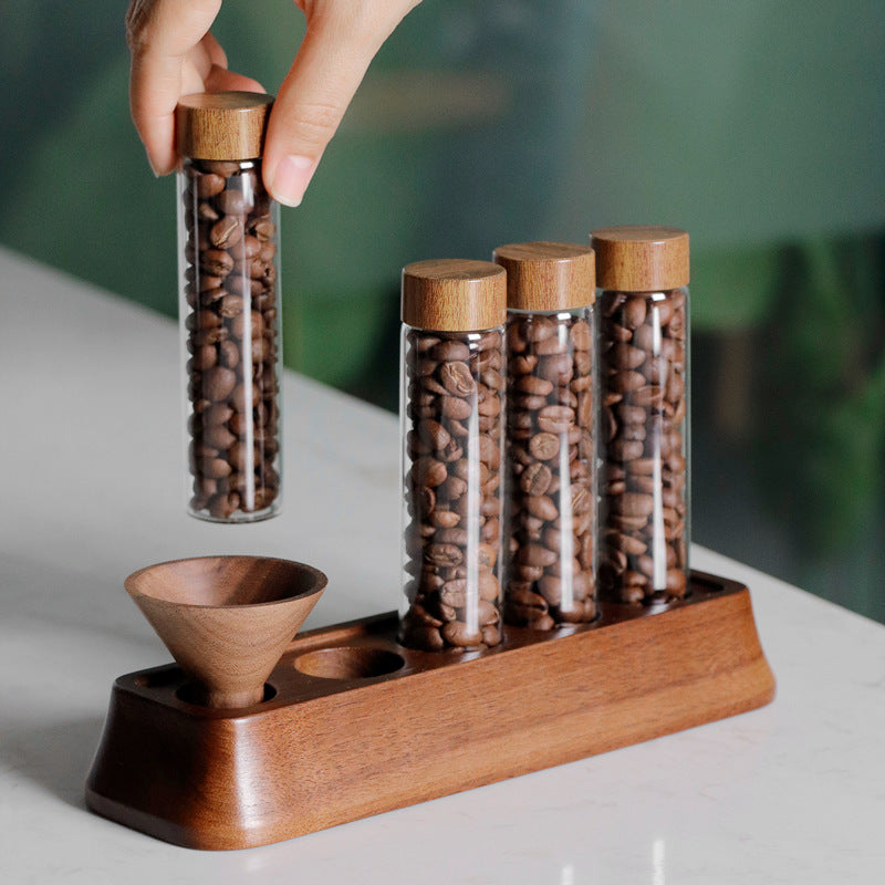 Glass coffee bean storage tube with cork lid, held above a wooden magnetic display stand